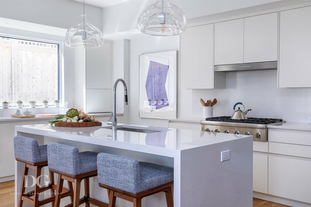 White waterfall kitchen island and blue upholstered stools and glass pendant lights