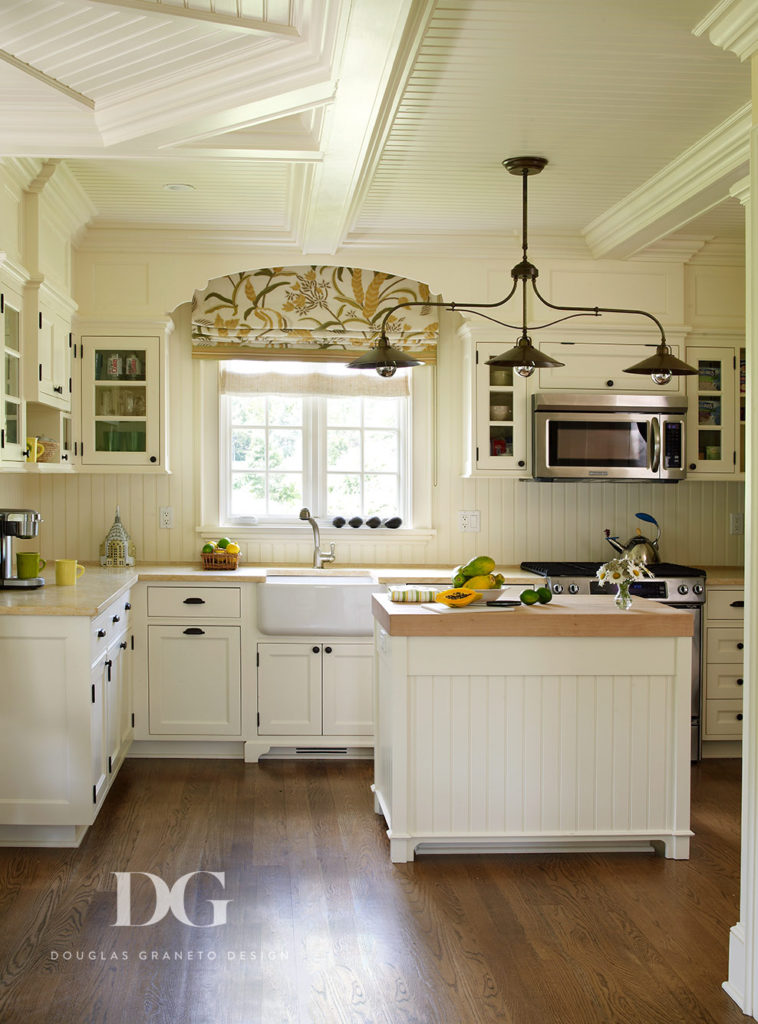 Spacious white kitchen featuring a hanging lighting fixture and other pieces from Chelsea Editions and Brunschwig & Fils.