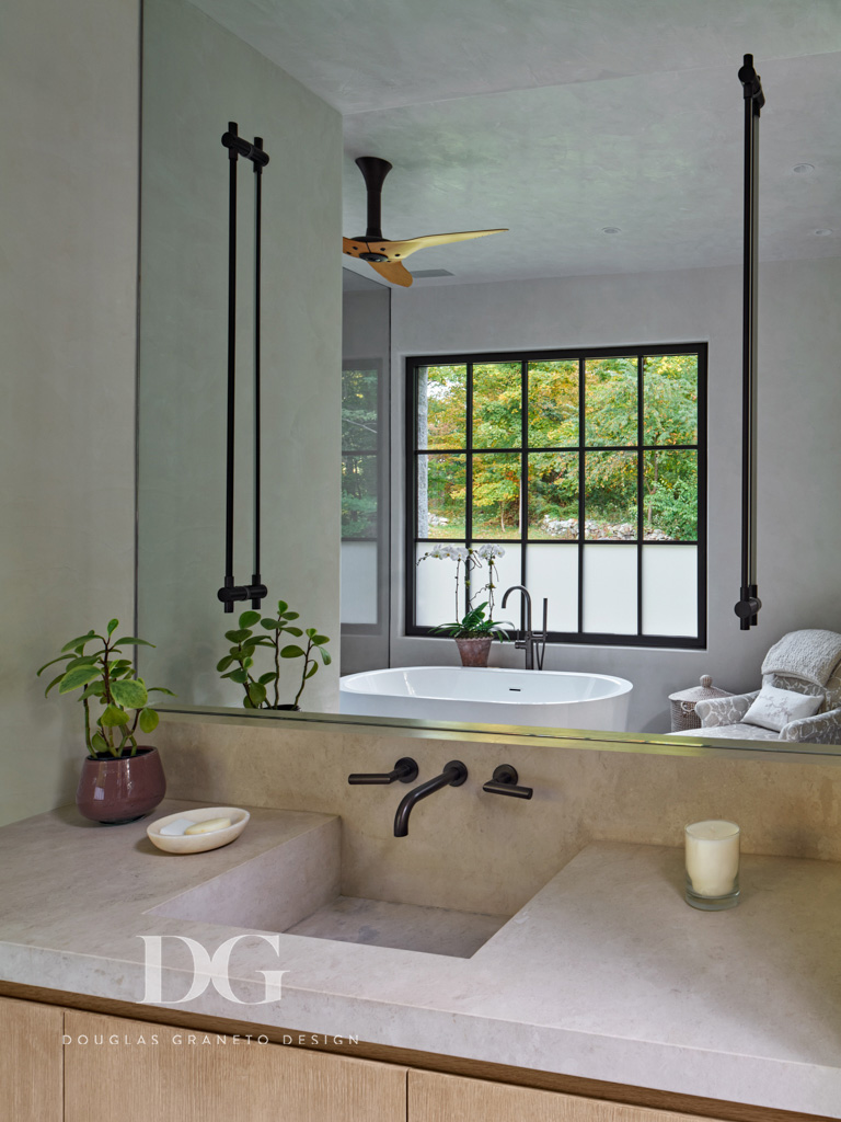 A custom stone bathroom sink with black faucet, a large wall mirror and sconces by Juniper