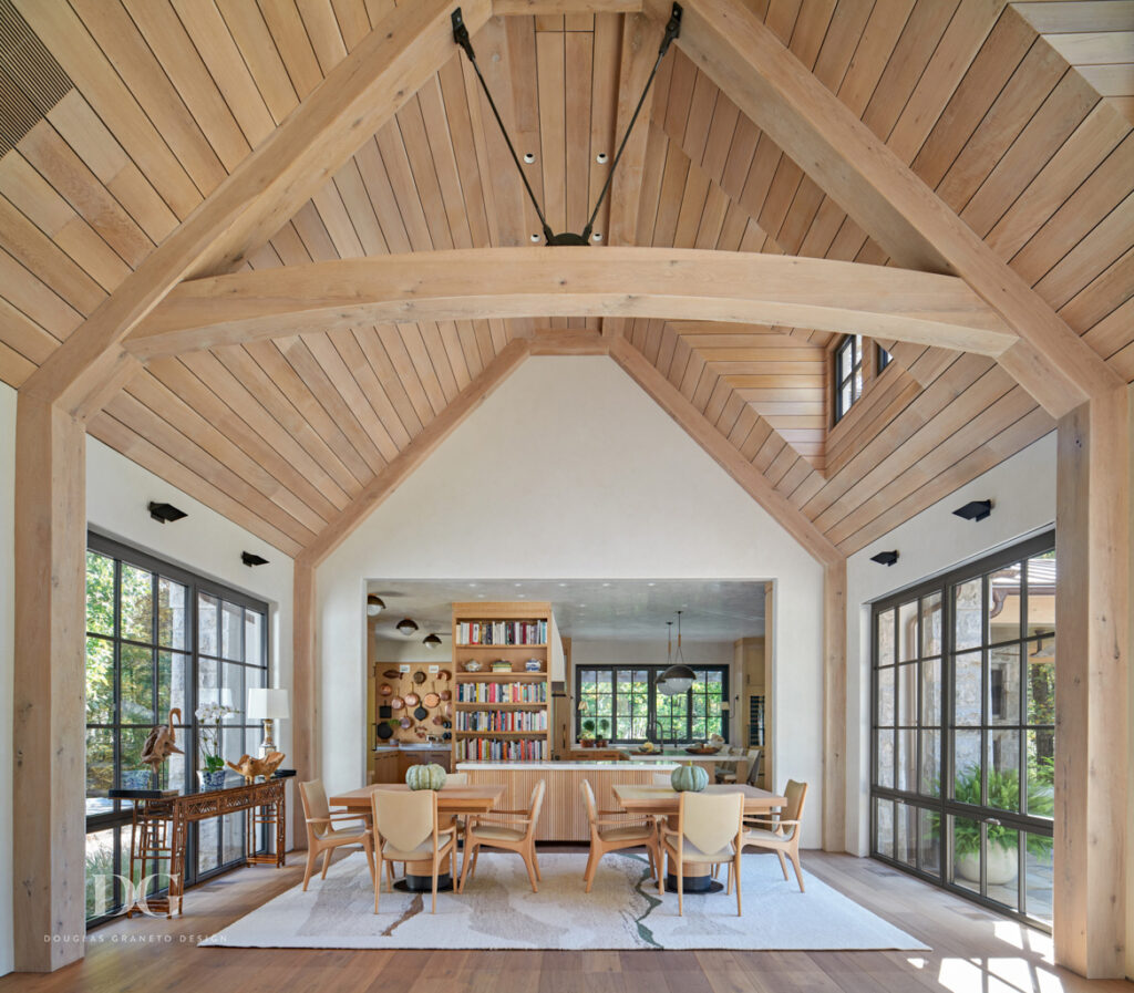 Wood paneled vaulted open plan dining area with custom kitchen in the background. Dining table and cabinetry by Rock Ridge Fine Cabinetry and chairs by Artistic Frame.