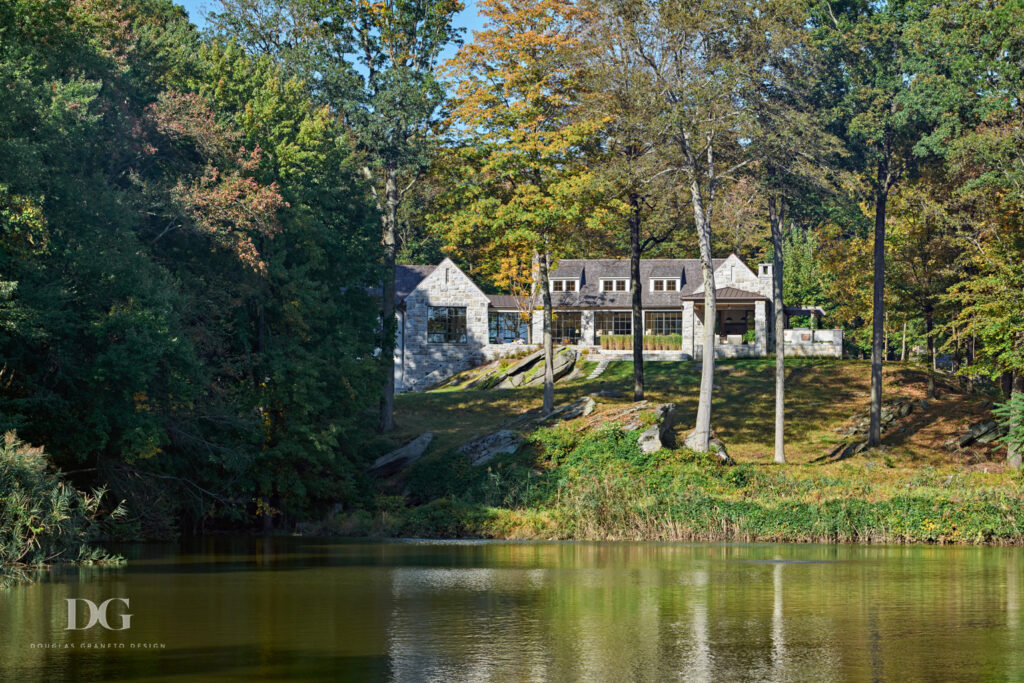 View across a pond of a stone clad house set amongst woodland