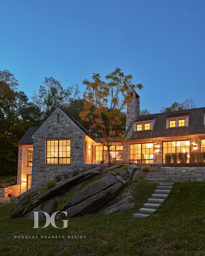 Nighttime view of stone clad house with large modern windows