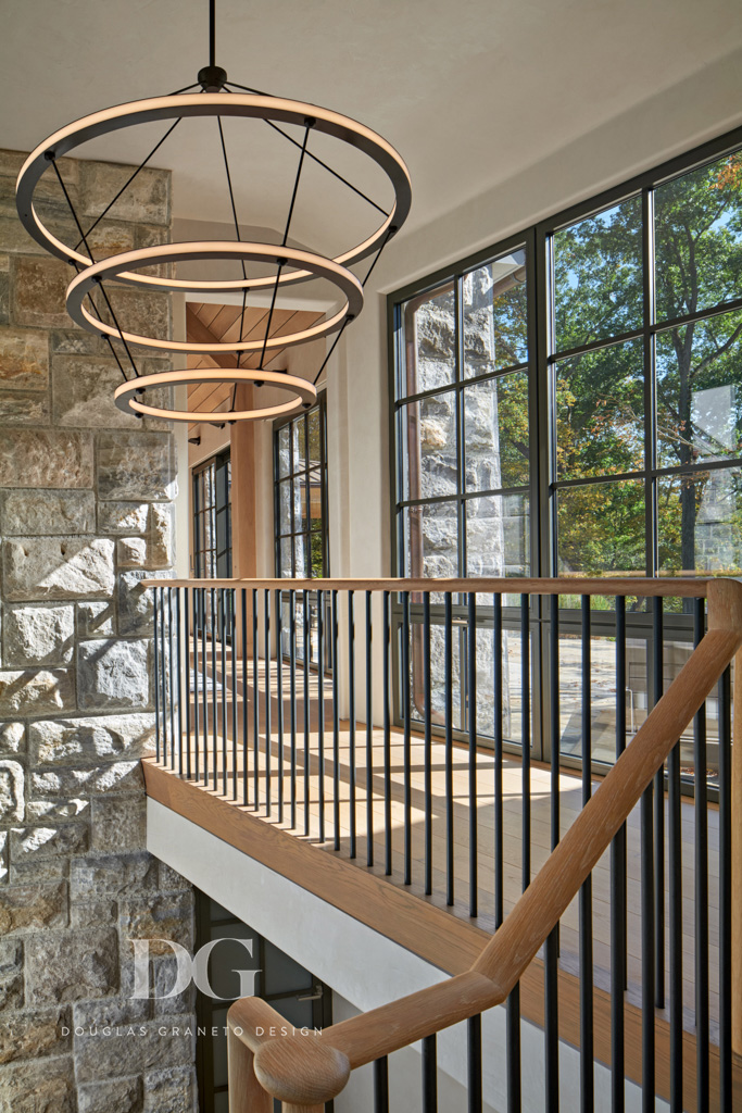 View of upstairs hallway from top of stairs showing black trimmed floor to ceiling windows and featuring a large Roll and Hill chandelier