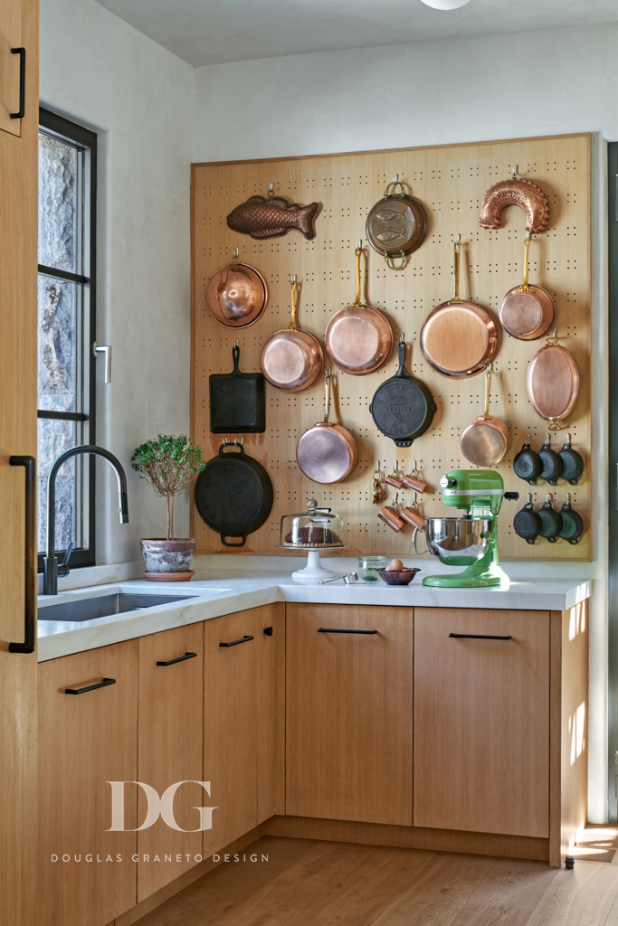 Corner of a custom pale wood and white kitchen with a peg board wall covered in copper pots. Cabinetry by Rock Ridge Fine Cabinetry and Millwork